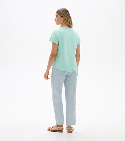 Back view of a sea glass short-sleeve V-neck tee with a relaxed fit and curved hem, worn with light pants.