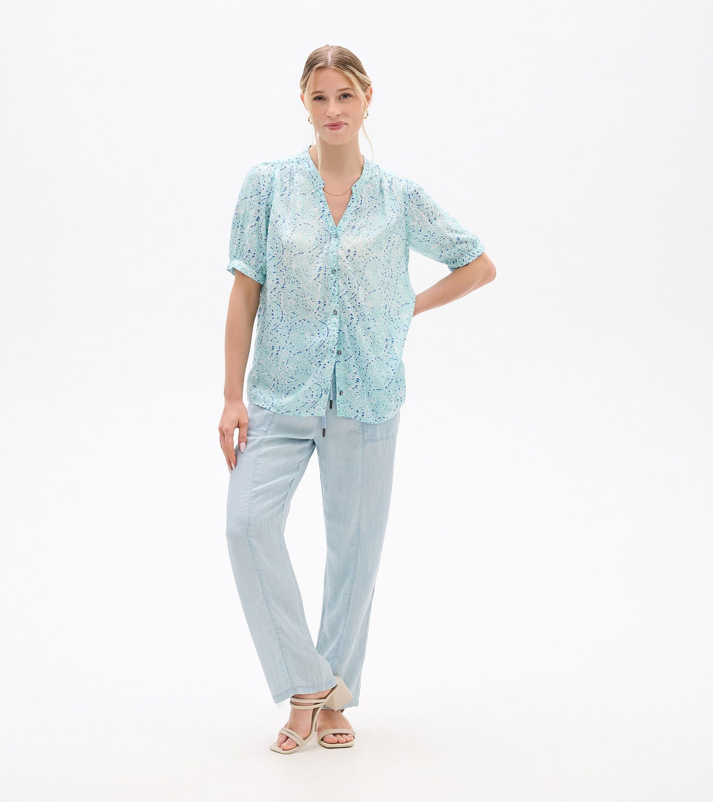 Front view of a light blue ikat-print blouse with short sleeves and button front, worn with pale pants.