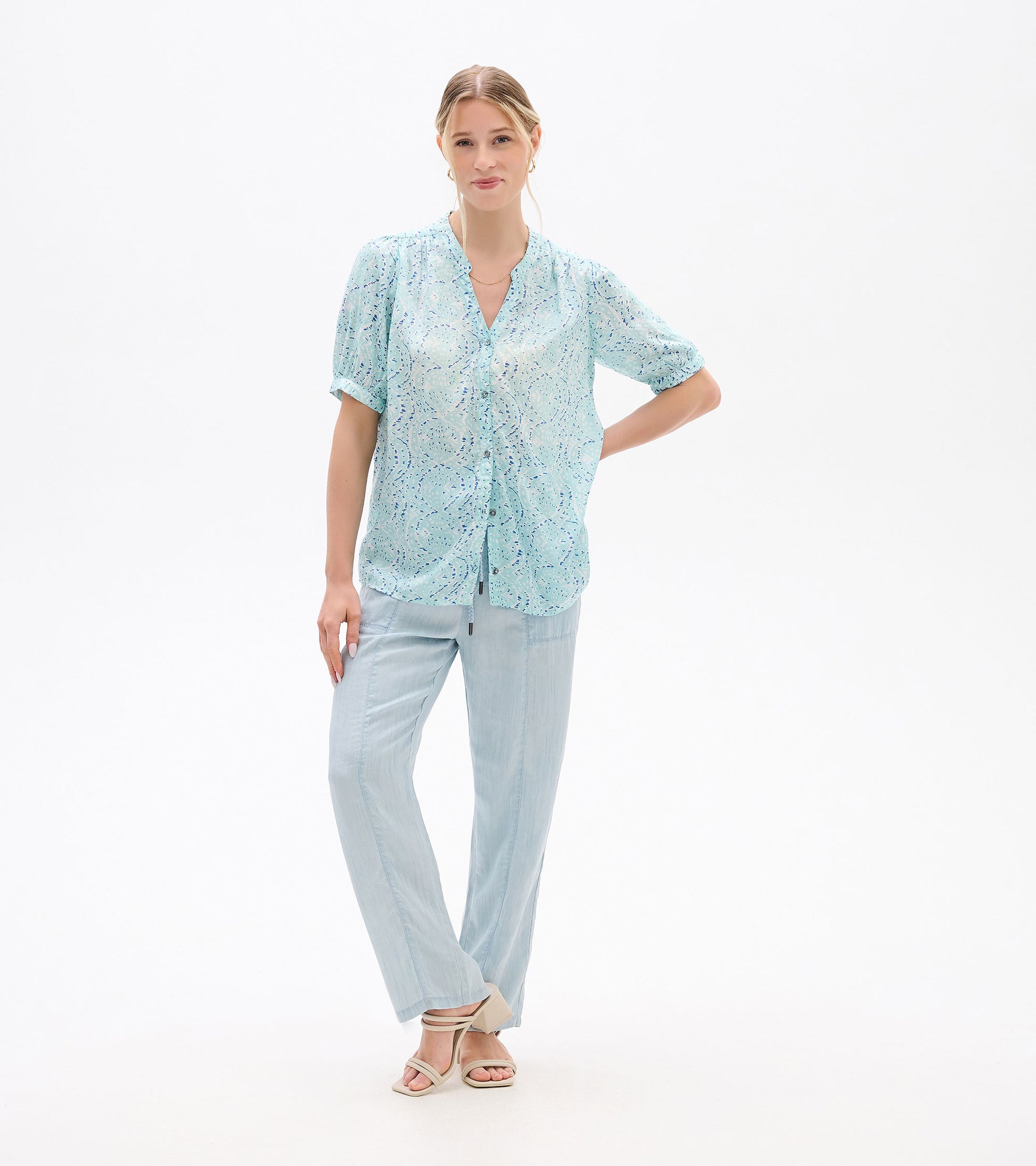 Front view of a light blue ikat-print blouse with short sleeves and button front, worn with pale pants.