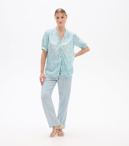 Front view of a light blue ikat-print blouse with short sleeves and button front, worn with pale pants.