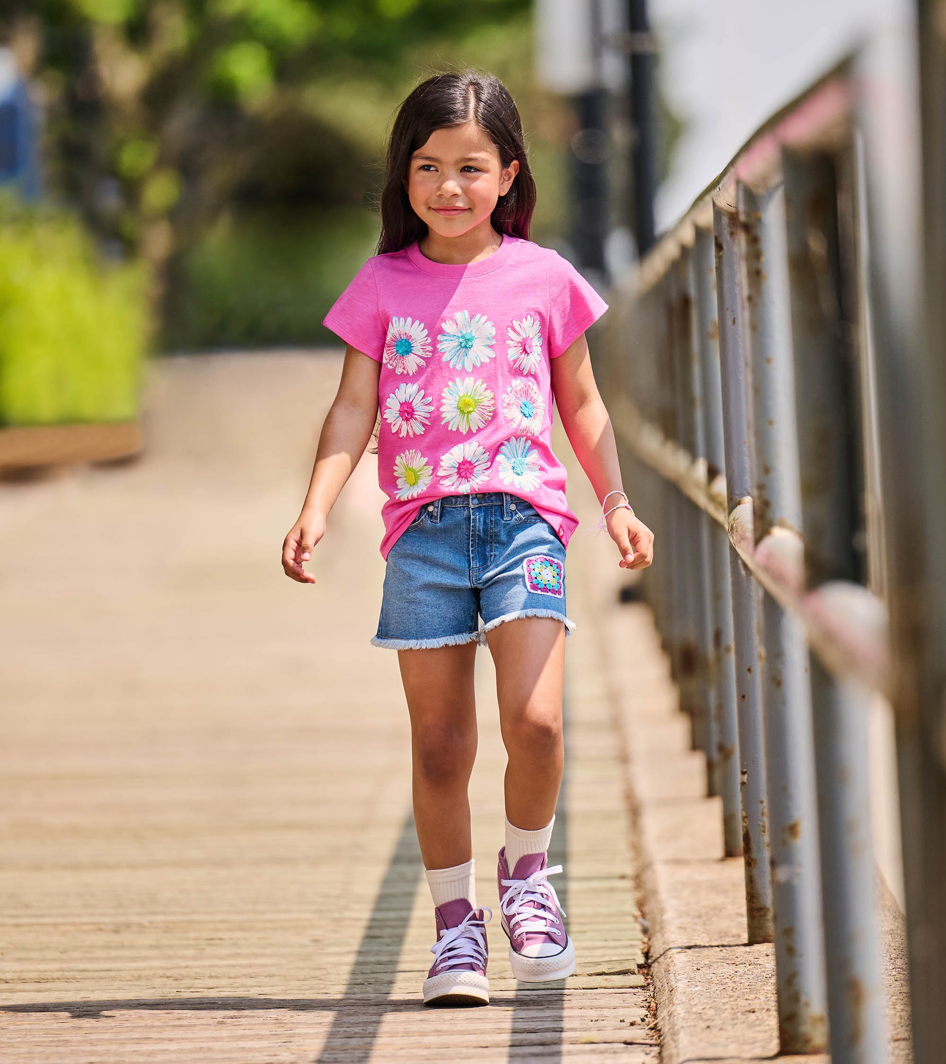 Girl wearing a bright pink crew neck tee with nine white flower graphics on the front