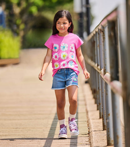 Girl wearing a bright pink crew neck tee with nine white flower graphics on the front