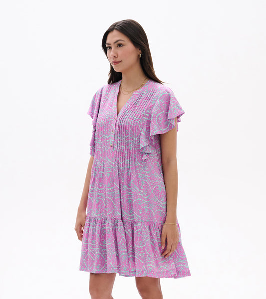 Front angled view of pink and light blue ikat pintuck dress with ruffle sleeves and tiered hem