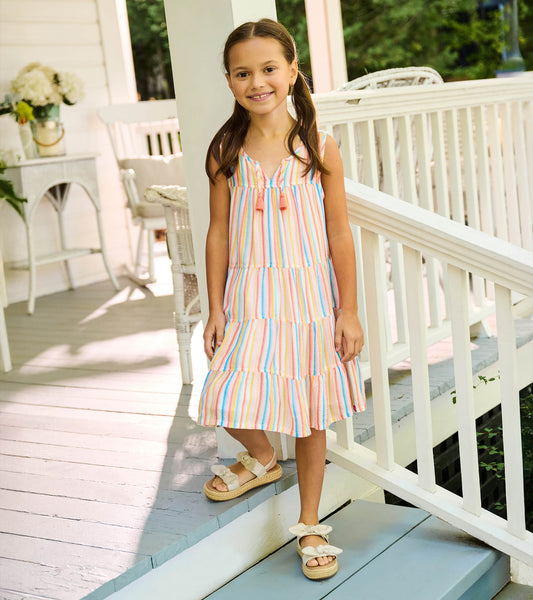 Girl wearing a sleeveless tiered dress with pastel vertical stripes and tassel ties at the neckline