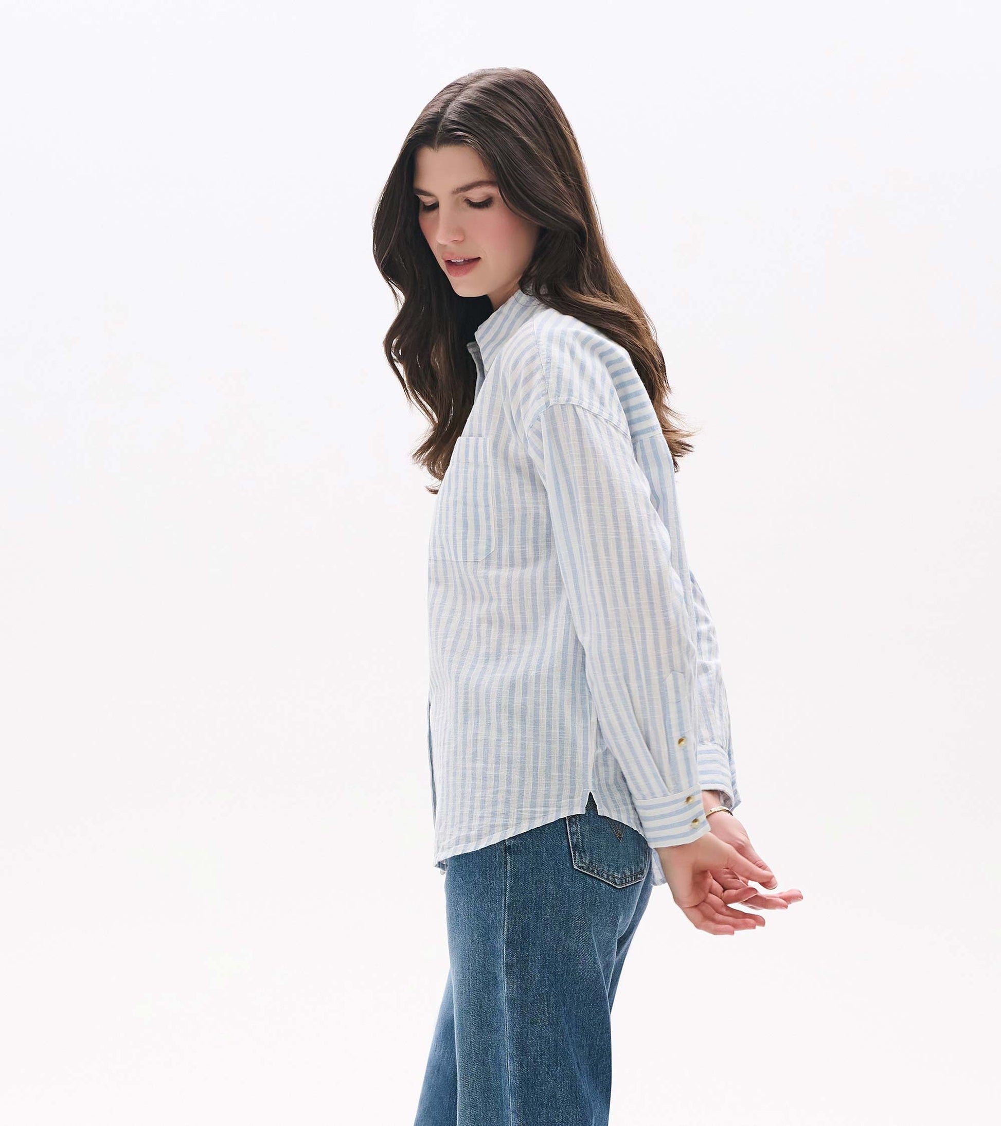 Side view of relaxed button-down shirt in pale blue and white stripes with chest pocket and curved hem