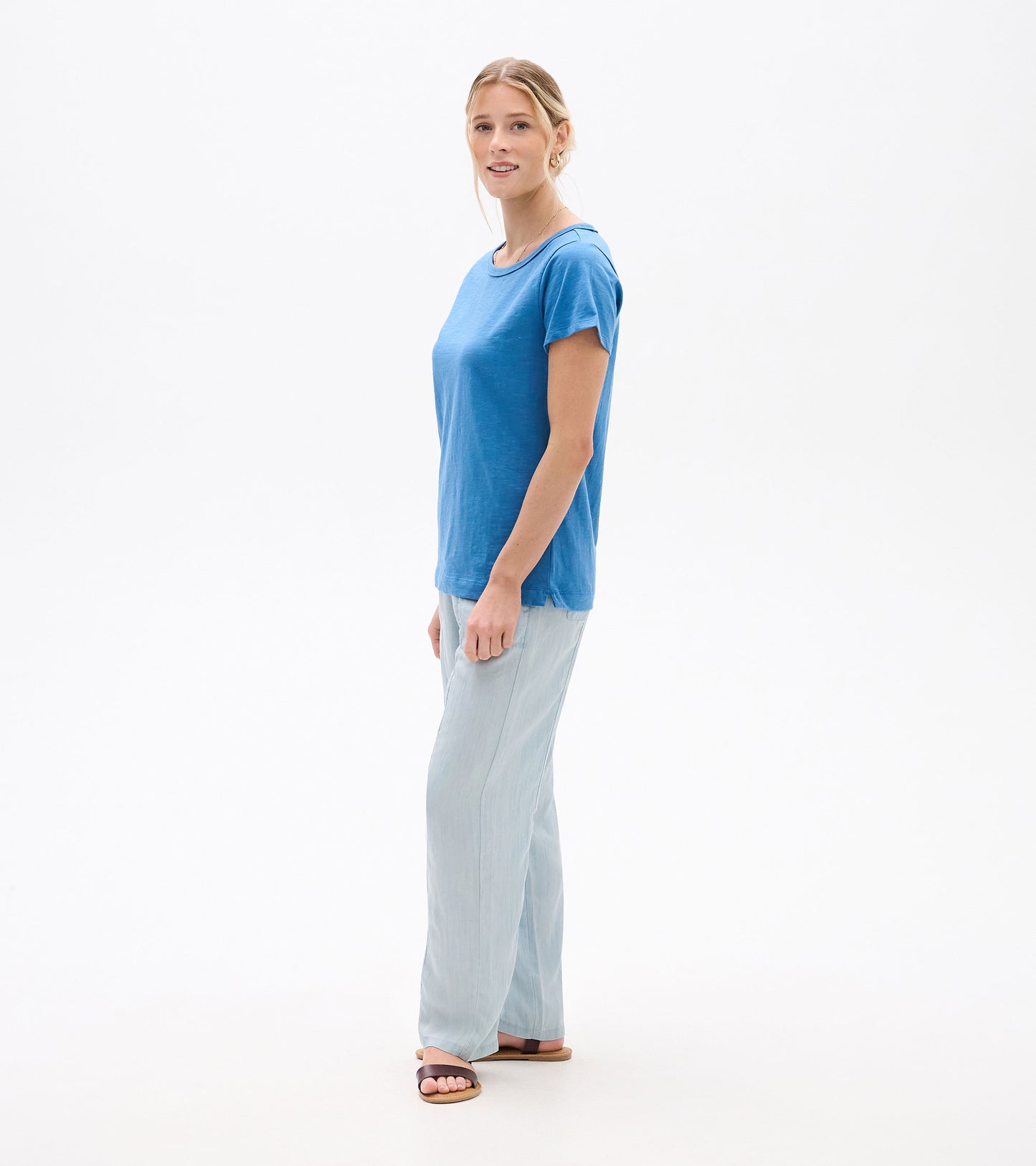 Woman wearing a solid blue crew neck short-sleeve tee, shown in side view.