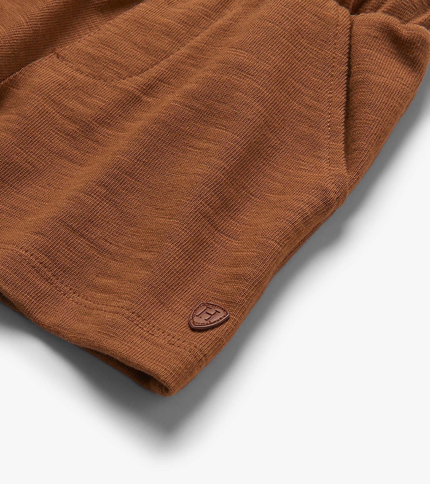Close-up of toasted coconut brown pull-on shorts with textured fabric and small logo patch at hem