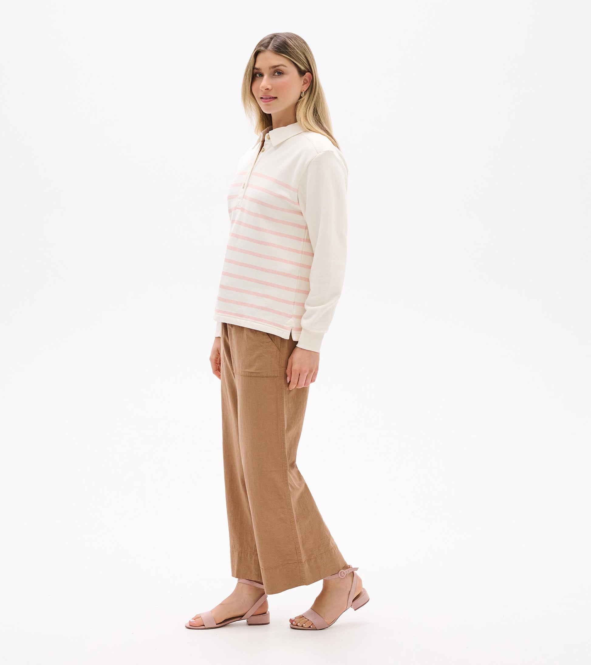 Cream long-sleeve polo top with pink stripes, collar, and button placket, shown on model in side view