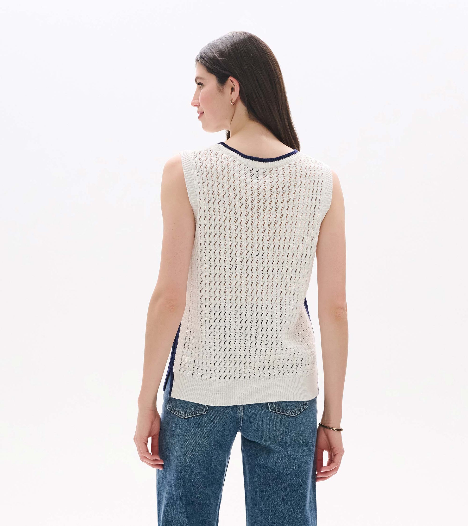 Back view of a white open-knit sleeveless tank with navy trim and ribbed hem, worn with jeans
