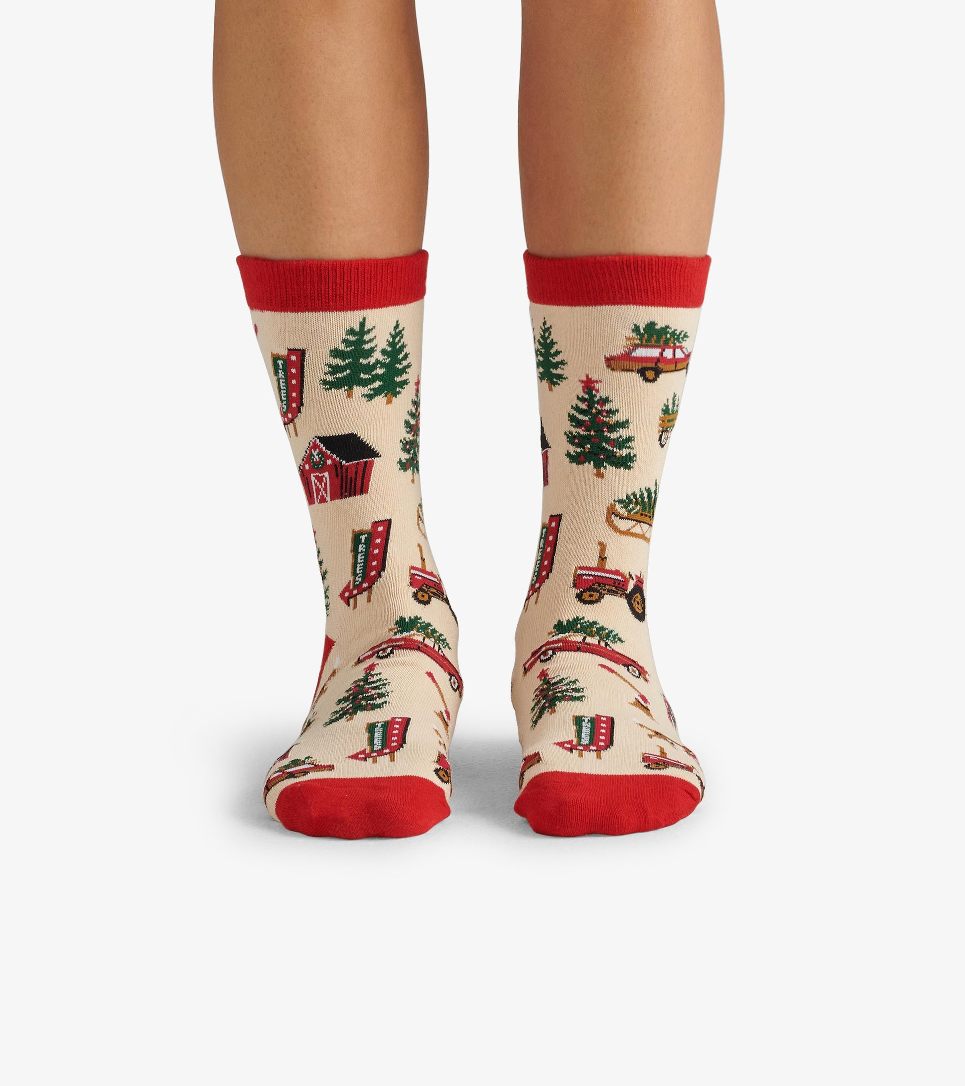 Beige crew socks with red cuffs featuring a Christmas tree farm pattern, including trees, tractors, and barns.