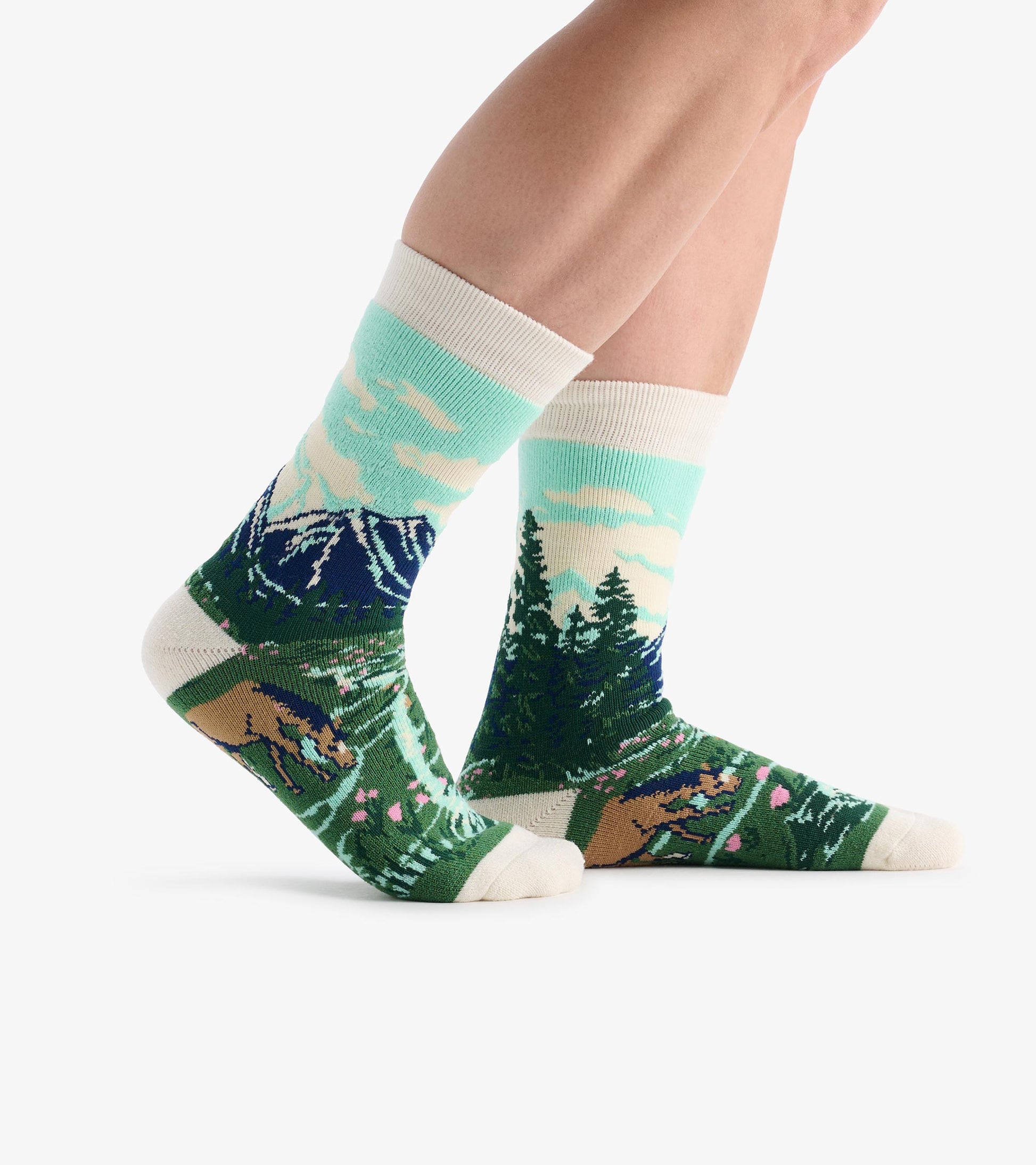 Crew socks with mountain, forest, and bear pattern in green, blue, and cream, shown on legs in side view.