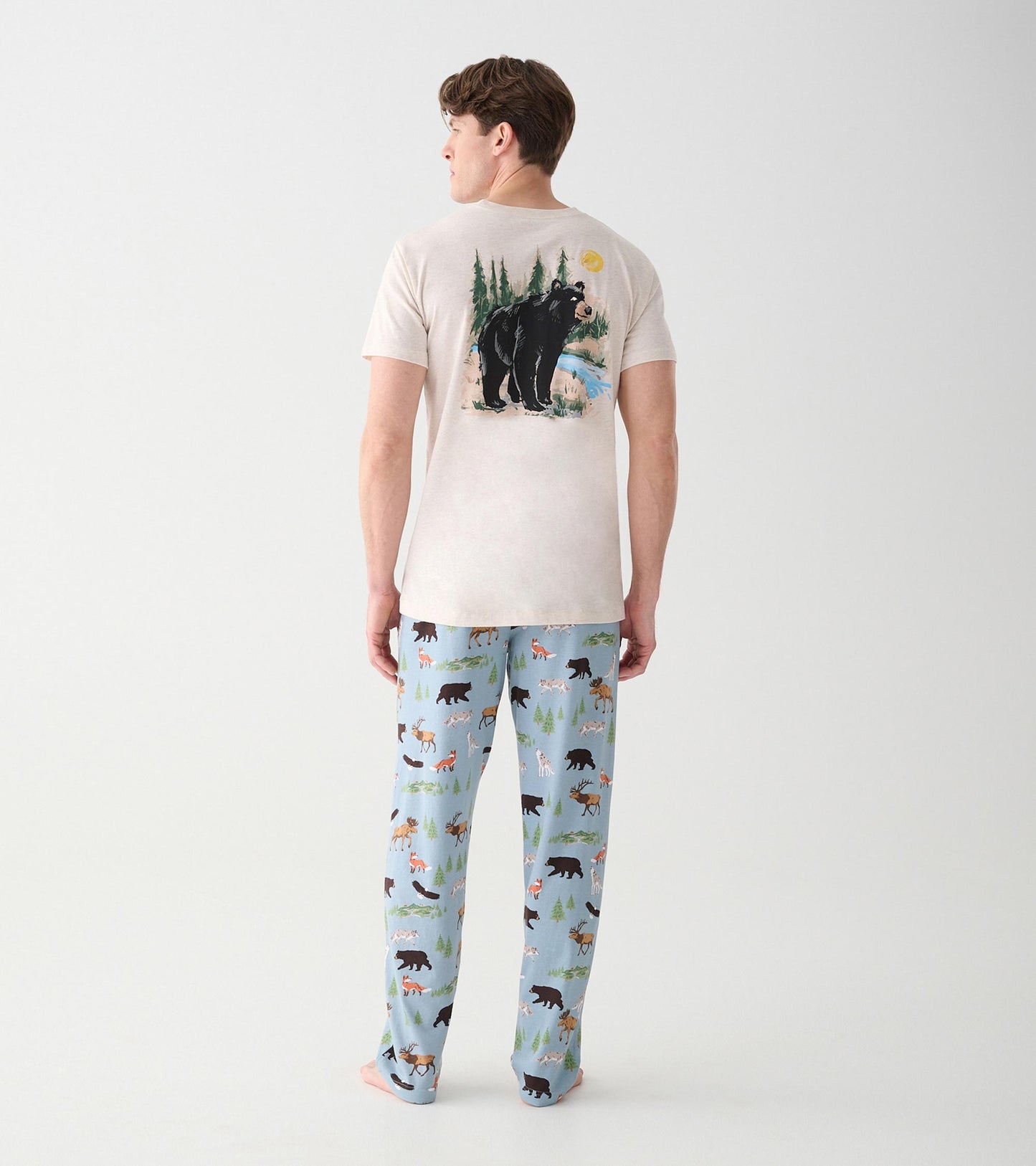 Full back view of oatmeal T-shirt with black bear wilderness graphic, worn with blue wildlife print pants