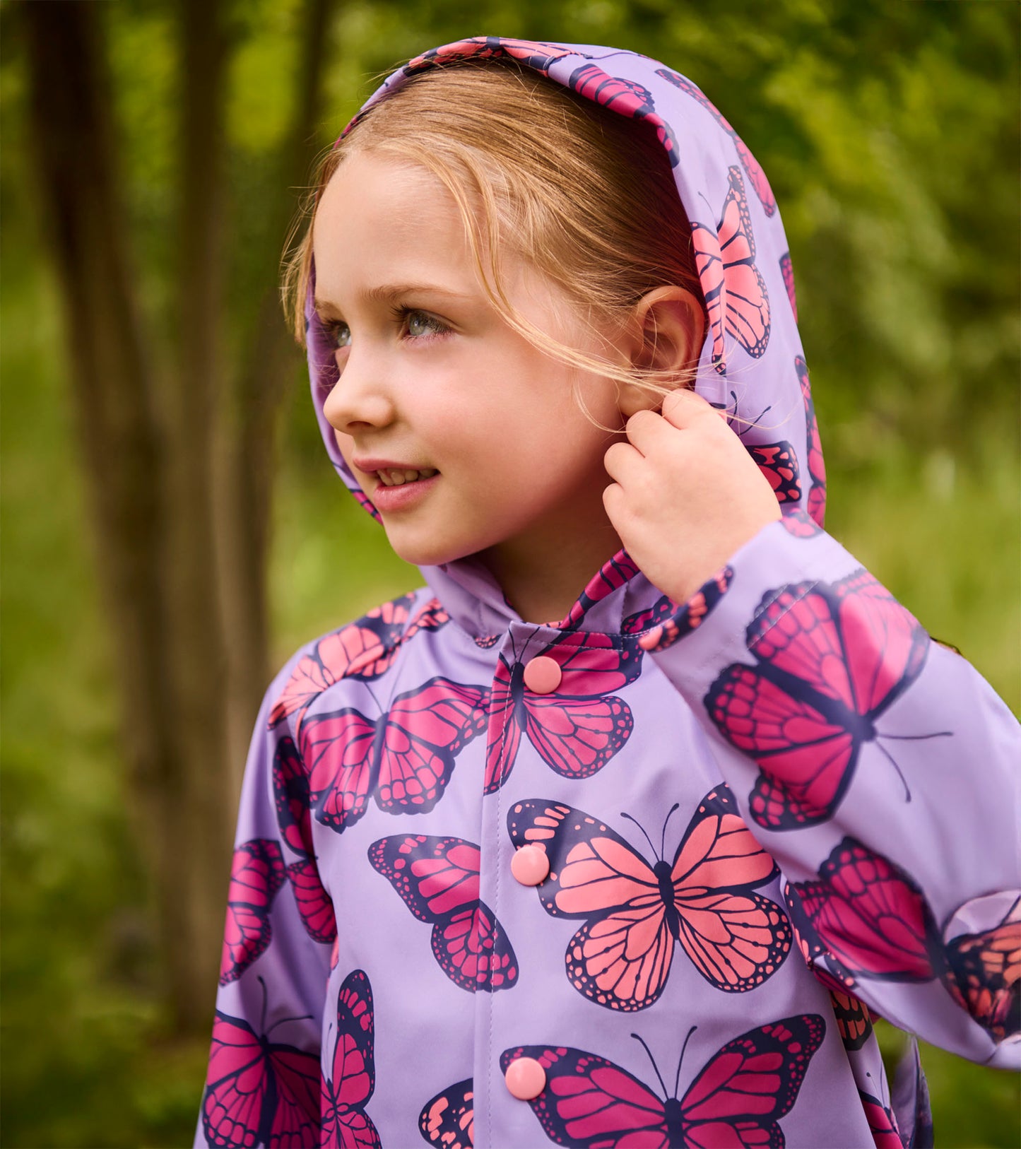 Girl wearing a lavender hooded rain jacket with pink butterfly print and snap buttons, front view