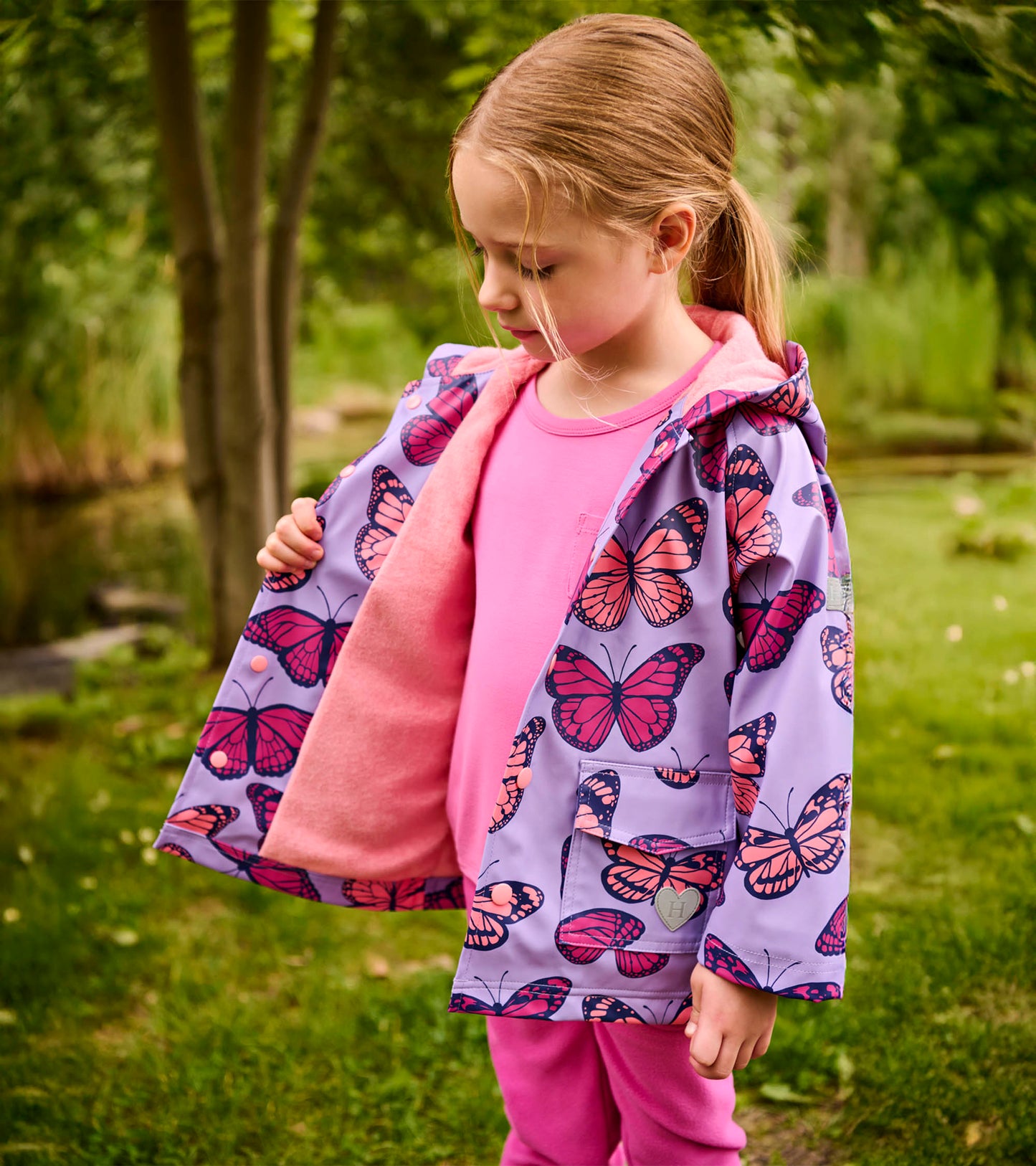 Girl wearing a lavender rain jacket with pink butterfly print and pink fleece lining, front view