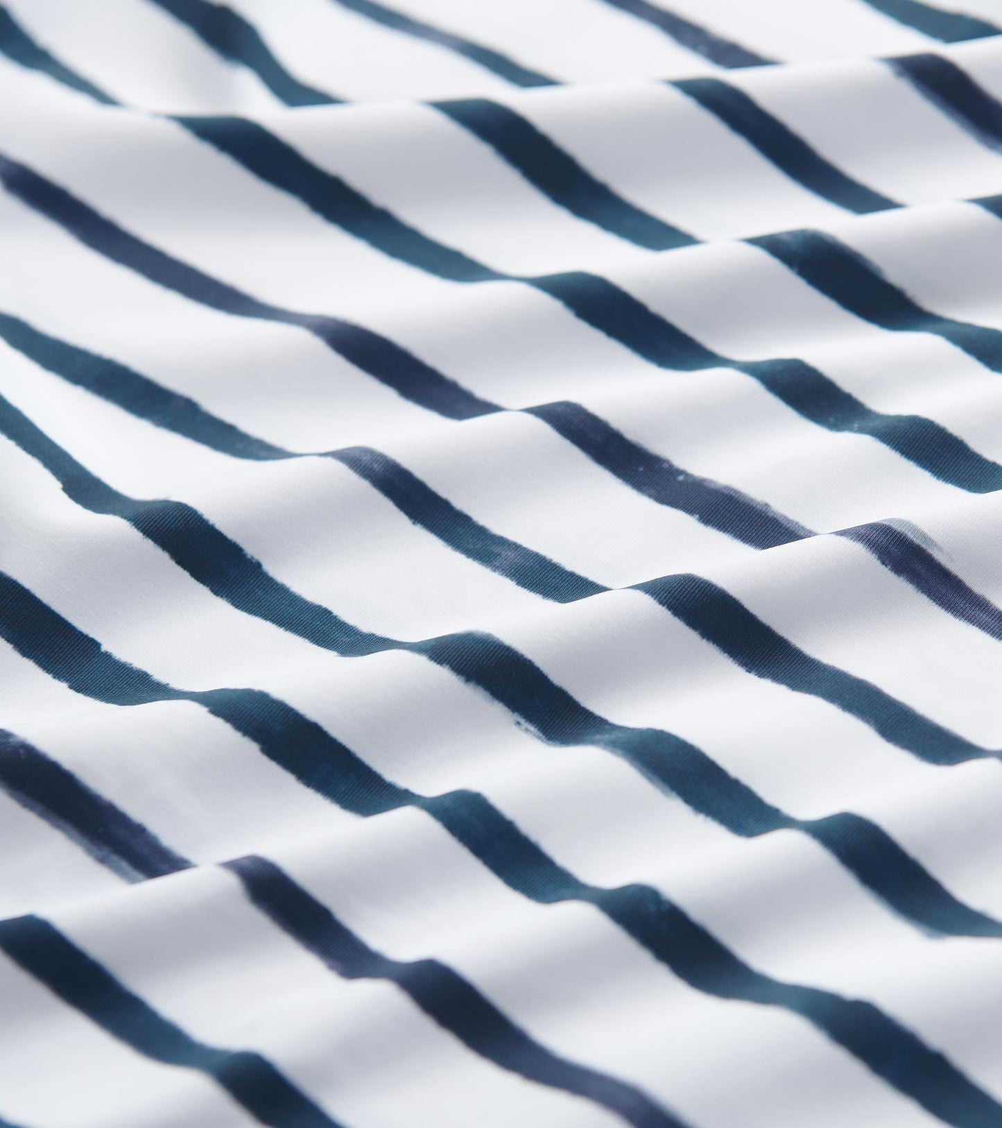 White fabric with navy watercolor stripes, showcasing a soft, flowing texture suitable for summer wear.