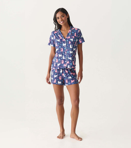 Woman wearing navy short-sleeve button-down pajama set with pink and white cat print and matching shorts.