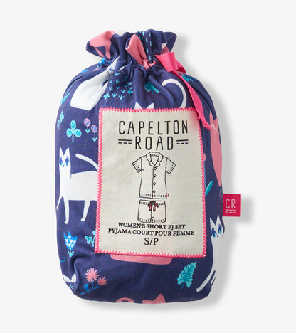 Folded navy pajama set with pink and teal cat print, tied in a drawstring pouch with label.