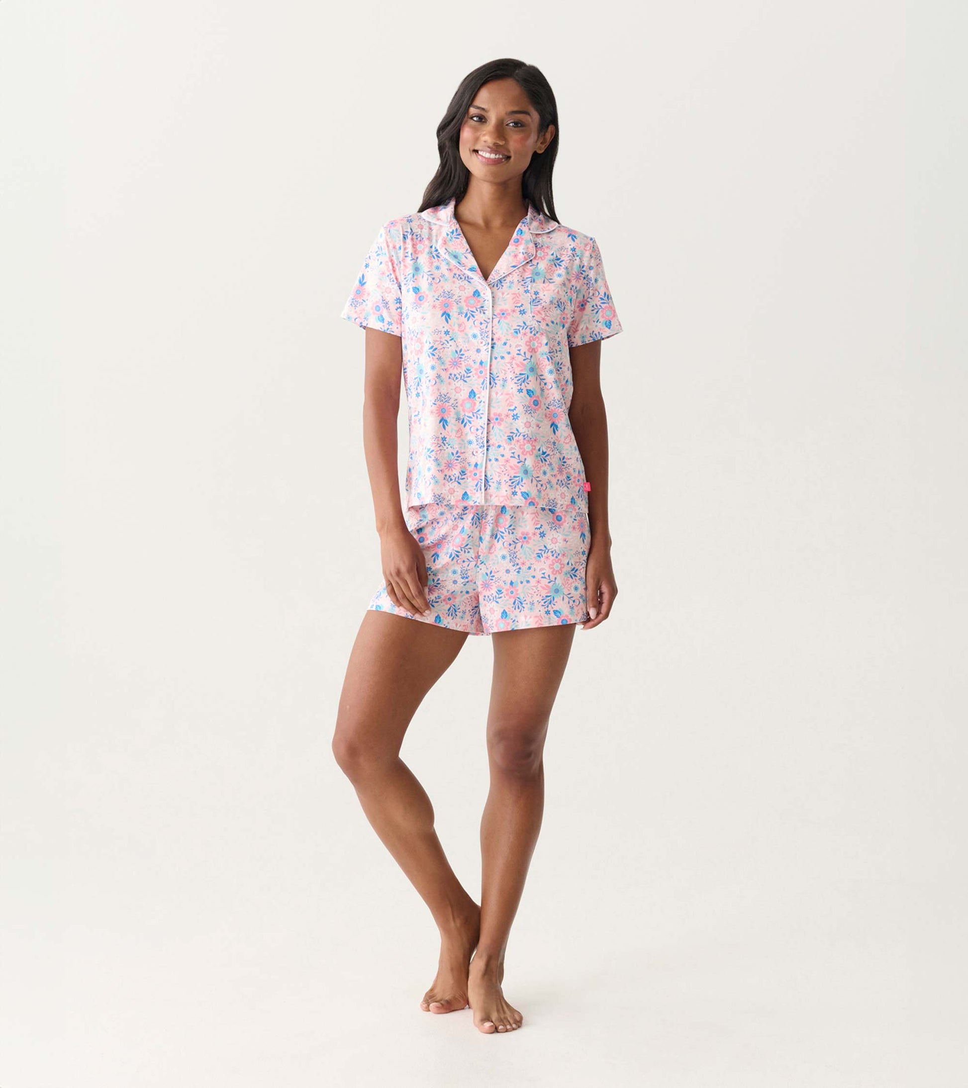 Woman wearing a pink and blue floral short-sleeve button-down pajama set with matching shorts, front view.
