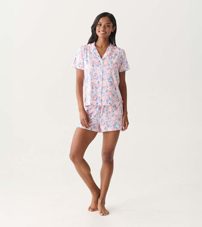 Woman wearing a pink and blue floral short-sleeve button-down pajama set with matching shorts, front view.