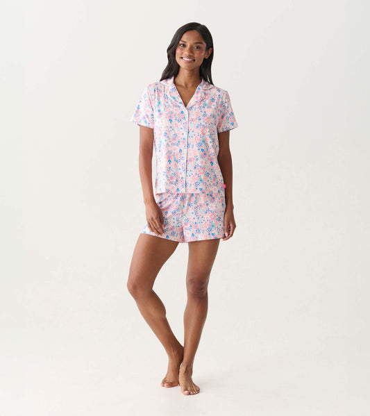 Woman wearing a pink and blue floral short-sleeve button-down pajama set with matching shorts, front view.