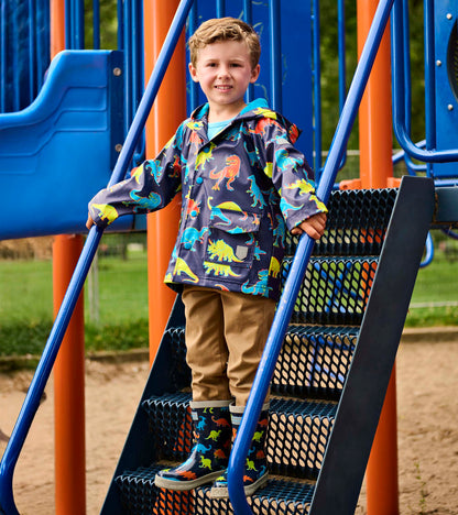 Boy wearing a navy hooded rain jacket with colorful dinosaur print, front view, on playground steps