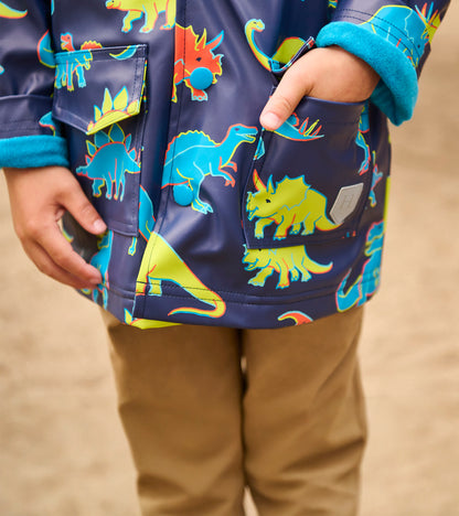 Front view of a navy rain jacket with colorful dinosaur print, flap pockets, and teal cuffs on a child