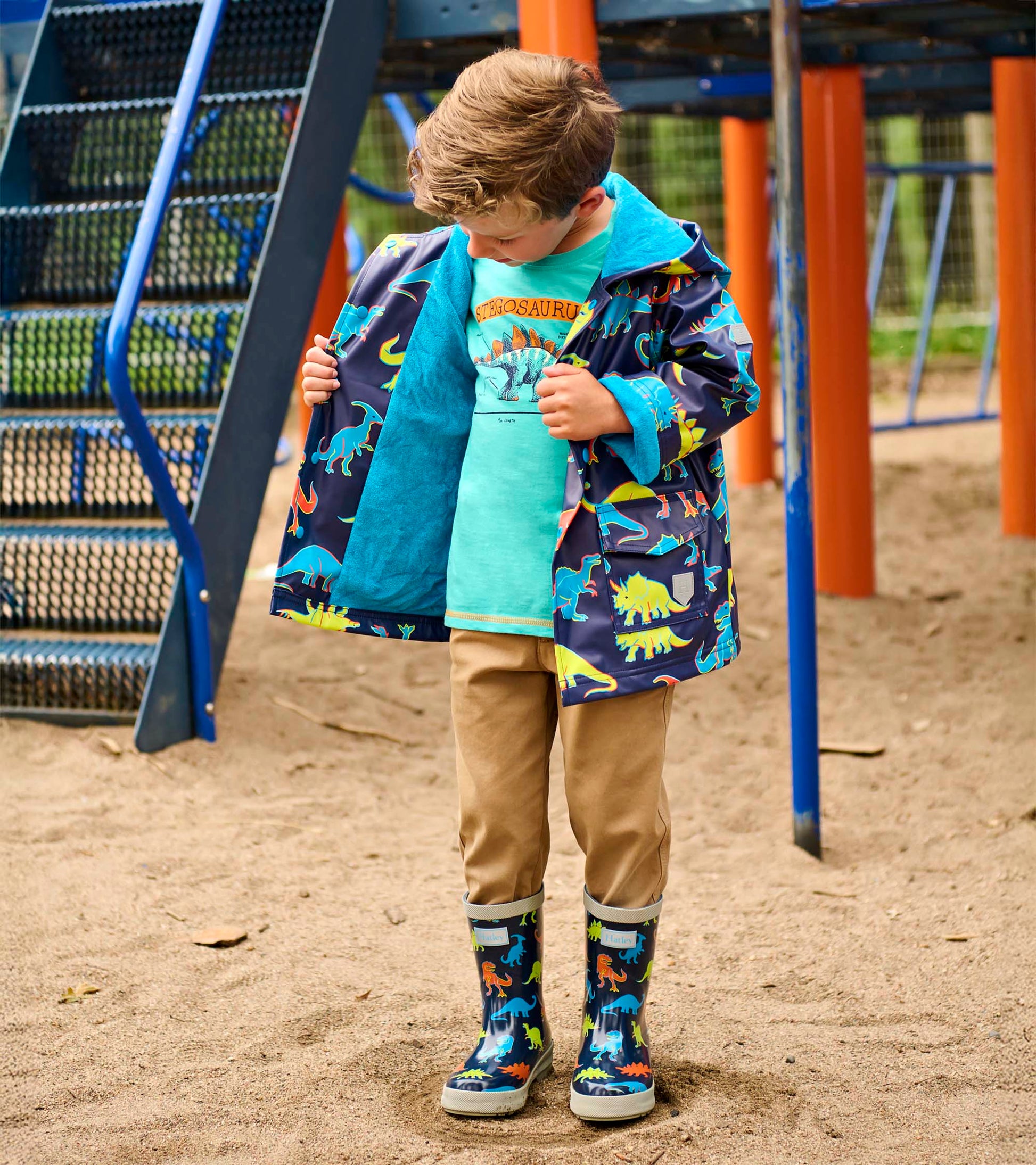 Boy wearing navy dinosaur-print rain jacket with turquoise lining and hood, open front view