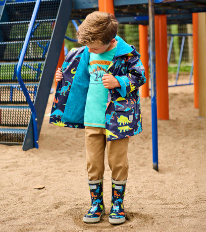 Boy wearing a navy dinosaur-print rain jacket with teal lining, open front, and hood at a playground