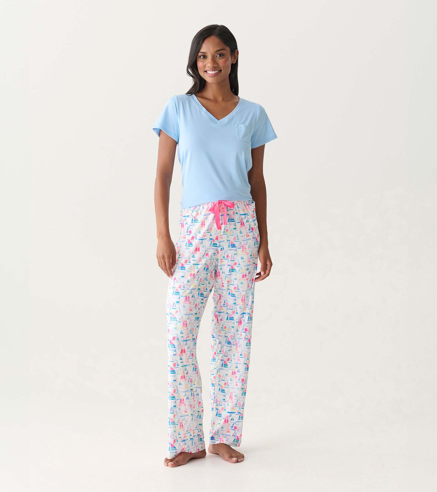 Woman wearing white pajama pants with colorful sailboat print and a light blue V-neck top, front view