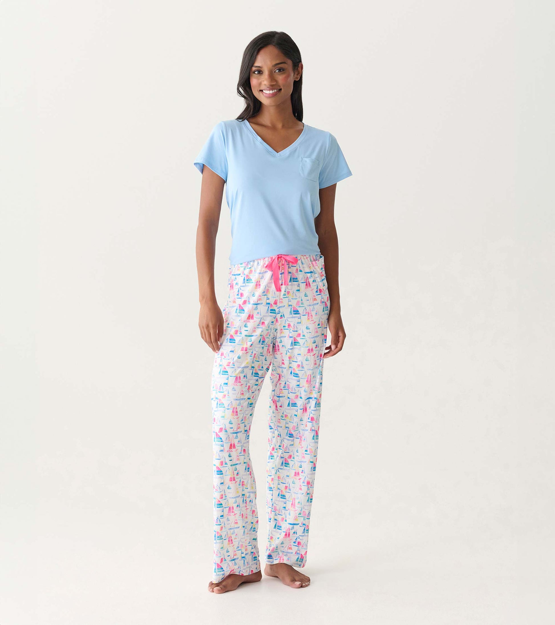 Woman wearing white pajama pants with colorful sailboat print and a light blue V-neck top, front view