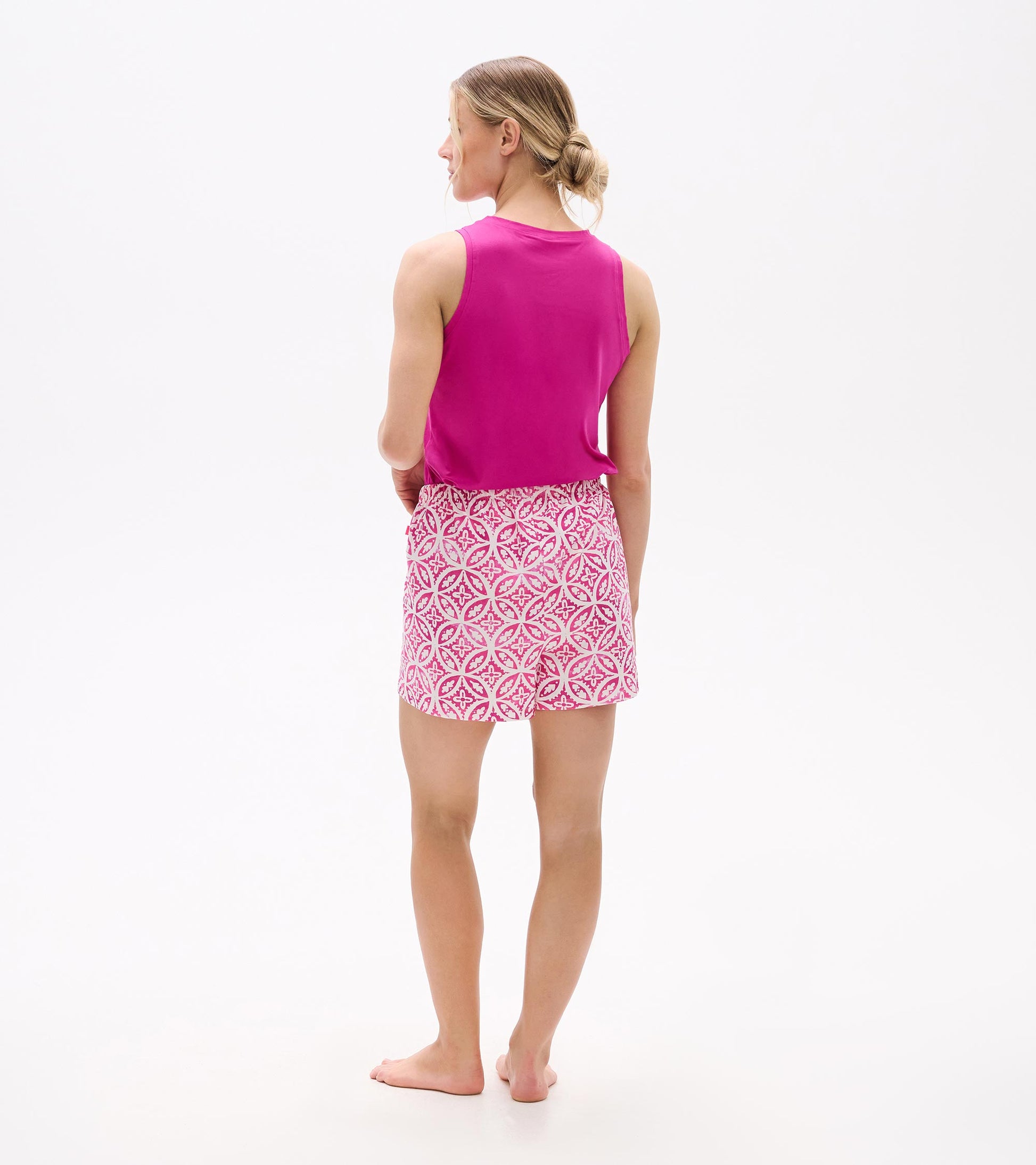 Back view of a woman wearing pink pajama shorts with a floral pattern and a matching pink tank top.