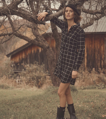 Black shirt dress with a white windowpane pattern, featuring a button-up front and long sleeves, styled with black boots.