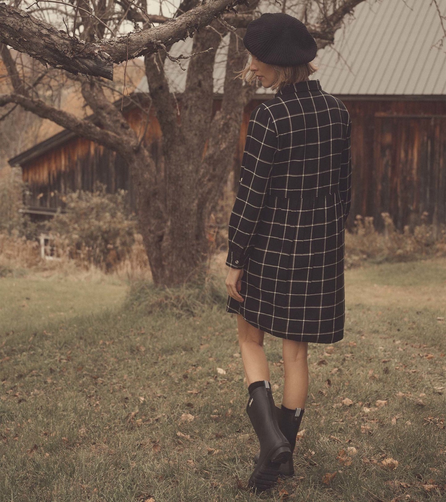 Black windowpane shirt dress with long sleeves, cinched waist, and a relaxed fit, worn with black rain boots.