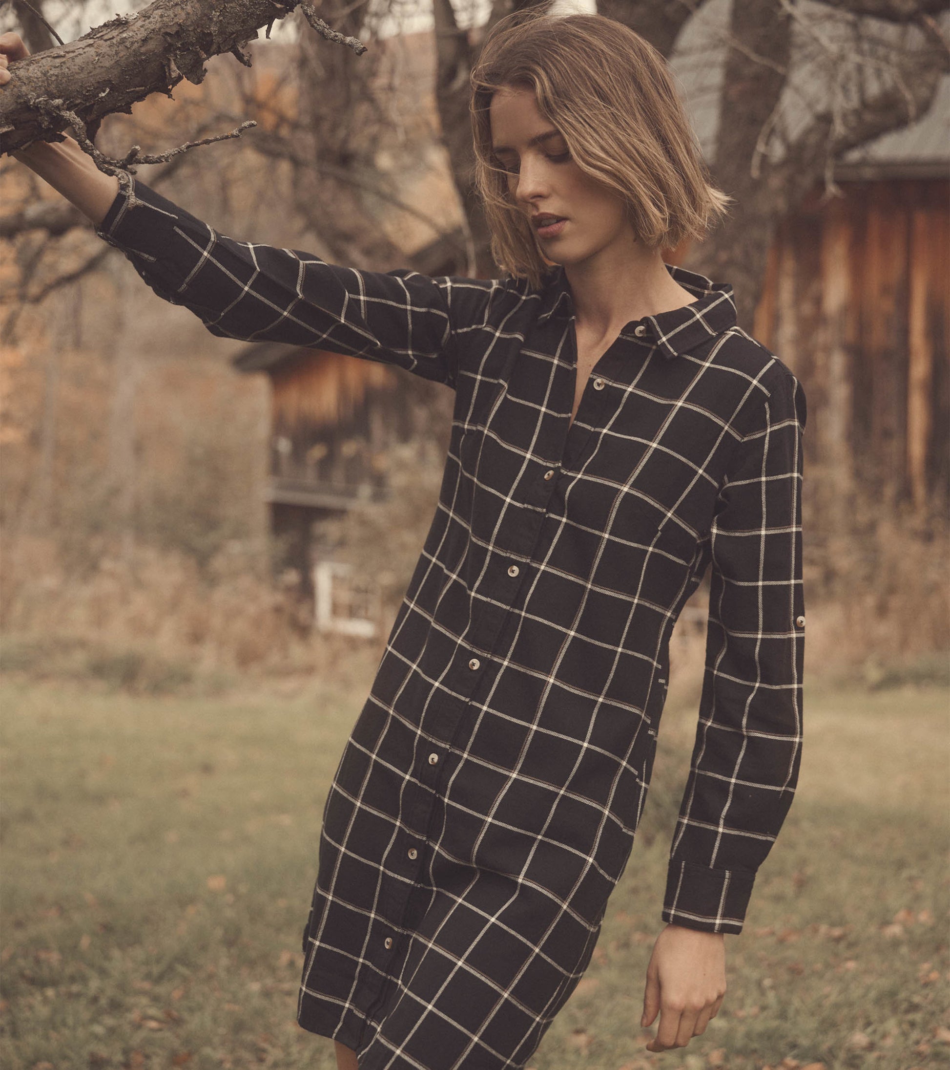 Black shirt dress with a white windowpane pattern, featuring a button front and long sleeves, worn outdoors.