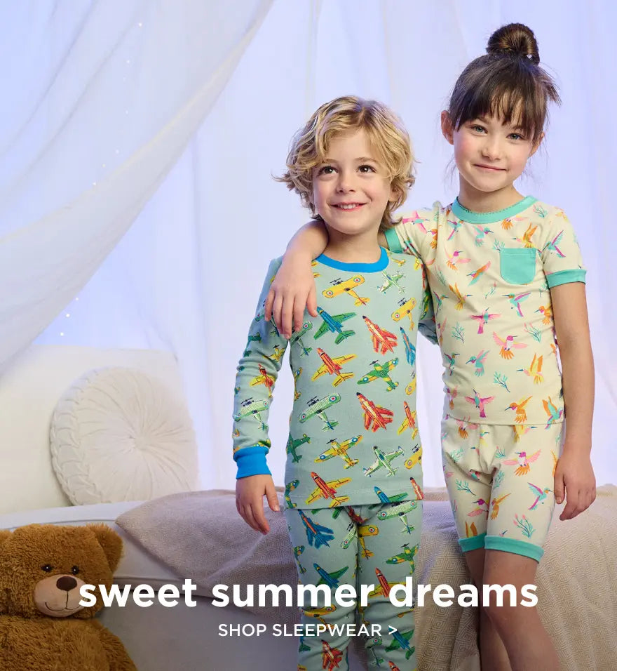 Promotes kids' sleepwear collection. Showing two children standing on a bed in patterned pajamas.
